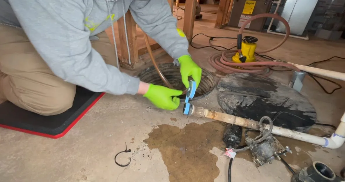 Worker replacing sump pump in basin, photographed during sump pump work in Chino Valley, AZ.
